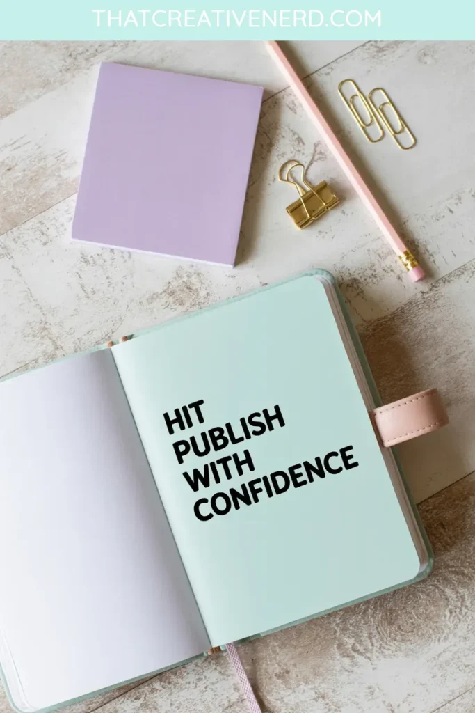 Flat lay of a pastel desk scene with a mint green open notebook displaying the phrase "Hit publish with confidence" in bold black text. Nearby are a pink pencil, purple notepad, gold binder clip, and paperclips on a whitewashed wooden surface.
