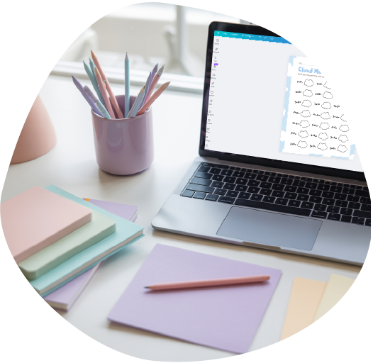 Pastel-themed workspace with a laptop displaying a printable “Cloud Math” activity, surrounded by stacked notebooks, a lilac pencil holder with pastel pens, and sheets of colored paper. The setup conveys a creative and organized atmosphere for planning or designing educational materials.